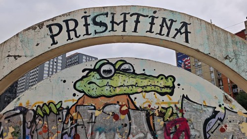 Graffiti of a cartoonish alligator under a large bow with the inscription Prishtina, Pristina,