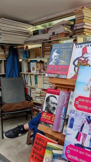Bookshelves in an outdoor bookstore with various books, Mein Kampf, and an empty chair, Pristina,