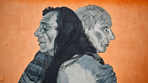 Large mural with two people hugging against an orange background, Pristina, Kosovo