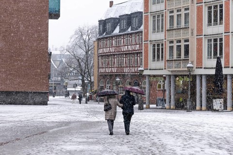 Two passers-by walk across Frankfurt's Römerberg with umbrellas. Heavy snowfalls have caused