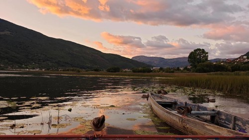 An old boat on a lake at sunset, with mountains and thick vegetation, Plav Lake, Montenegro