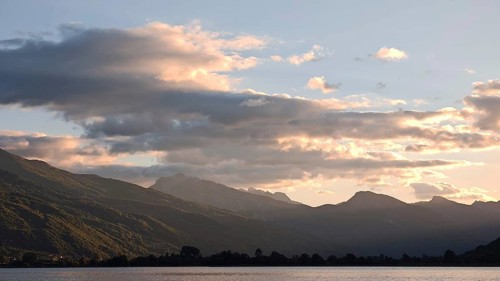View of a mountain range with clouds glowing over a calm lake in the evening light, Plav Lake,