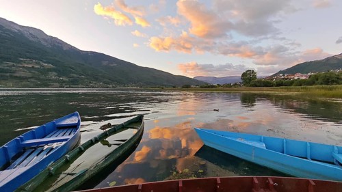 Three colorful boats on a calm lake at sunset surrounded by mountains and cloudy sky, Plav Lake,