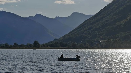 A boat with two people on a lake surrounded by mountain silhouettes in the evening light, Lake