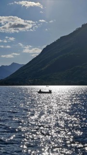 A lonely boat on a sparkling lake with mountains in the background and sunny atmosphere, Lake Plav,