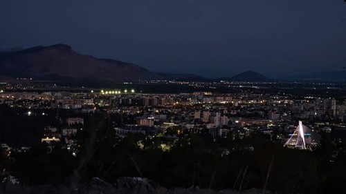 Nighttime city view with illuminated buildings, mountains in the background and dark sky,