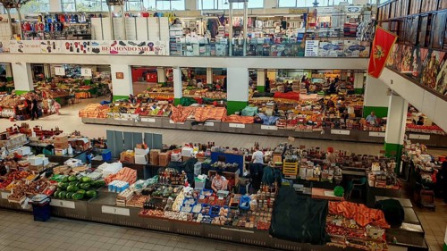 Large market hall with numerous stands and products. People buy fresh food. Lively atmosphere,