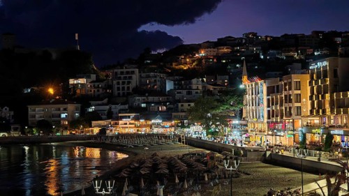 A nighttime beach view with illuminated buildings and dark skies in a lively coastal town, Ulcinj