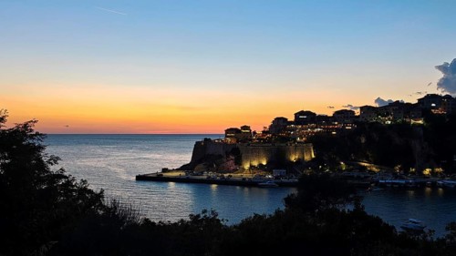 Sunset over a coastal town with silhouetted buildings and a calm sparkling sea, Ulcinj, Montenegro