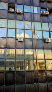 Reflections of clouds and cranes in a glass façade of a high-rise building, Pristina, Kosovo