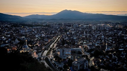 Night view of city with glowing lights, river and mountain skyline in the background, Prizren,