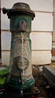 Old green hydrant with Victoria inscription with water flow in front of a wall, Kosovo