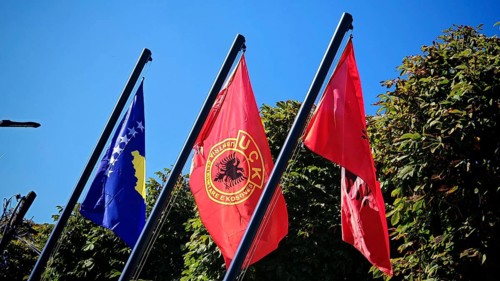 Three flags of Kosovo, USK, Albania fly against green background and blue sky, Kosovo