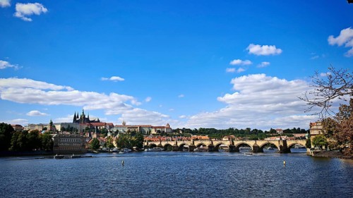 Panorama of a bridge and surrounding architecture along a river under a blue sky, Prague, Czech