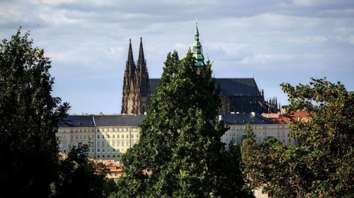 Gothic church between tall trees, cloudy sky in the background, view of Hradcany, Prague, Czech