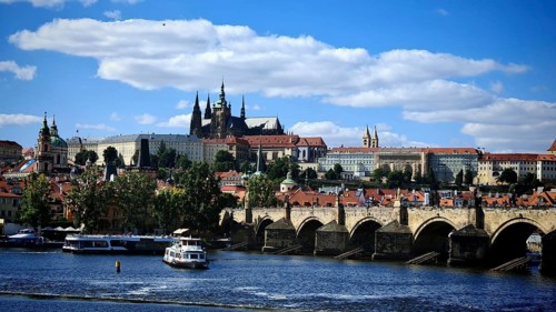 Historic bridge over a river with impressive architecture in the background under blue sky, view of