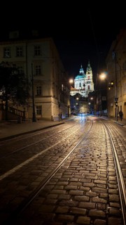 Illuminated cobblestone street with tram tracks at night with a view of a cathedral, Prague, Czech