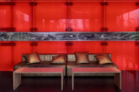 Sofa with golden cushions in front of a red-illuminated glass wall, stylish lobby of an apartment