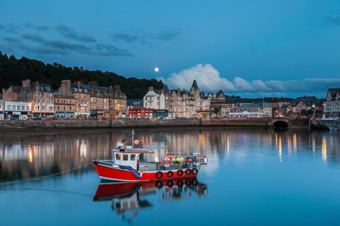 Oban, Argyll and Bute, Scotland, UK. A red traditional fishing boat in the port of Oban and old