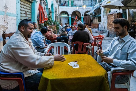 Tripoli, Libya, North Africa. Man playing cards and others smoking shisha in a traditional 'funduq'