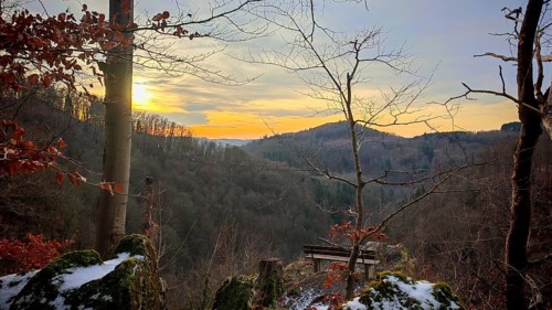 A sunset with a bench with a view over a forest with trees and rocks with snow, Franconian Forest