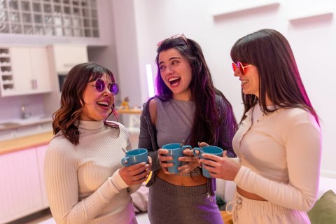 Three smiling young women friends wearing stylish sunglasses and casual clothes sharing a happy