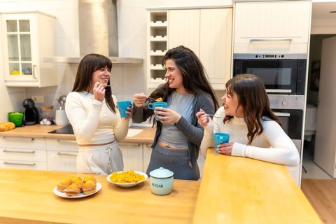 Three smiling young women friends enjoying breakfast together, eating cereal and muffins, drinking