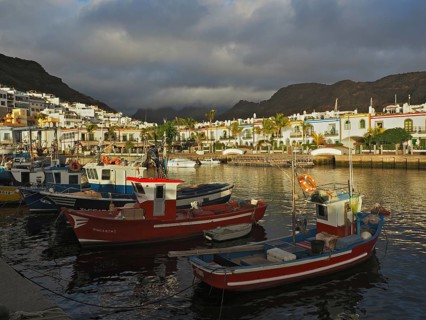 Fishing boats in quiet harbor with colorful houses in soft evening light, Puerto de Mogan, Gran