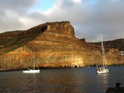 Rocks on calm sea with boats and golden evening sun, Puerto de Mogan, Gran Canaria, Canary Islands,