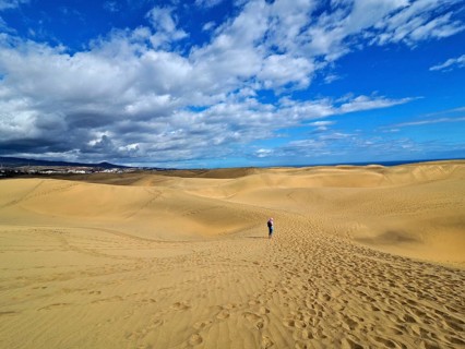 Large dune landscape with footprints and a hiker under a blue sky with white clouds, dunes of