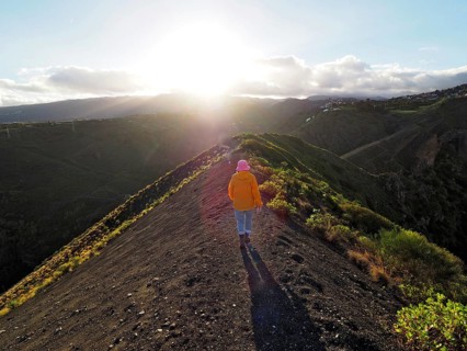 Female hiker walks along a sunlit hill with extensive shadows, Caldera de Bandama volcanic crater,