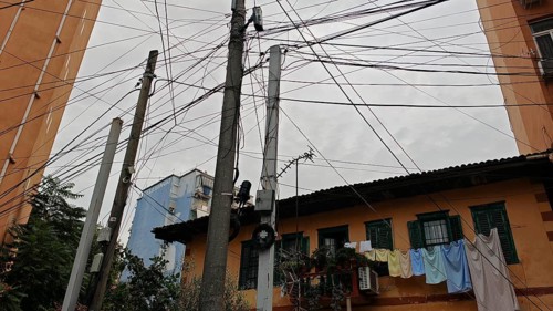 Power poles with a tangle of wires, next to buildings and clotheslines, create an urban image,