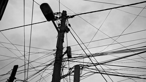 Black and white shot of numerous wires twisting around a power pole against a cloudy sky, Tirana,
