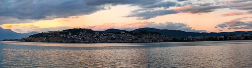 Evening panorama of a lake with mountains and a city in the background under dramatic sky, Lake