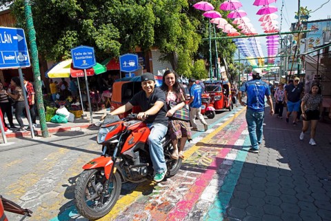 Mayans wearing traditional and modern clothes on a motorcycle in an alley in San Juan la Laguna,