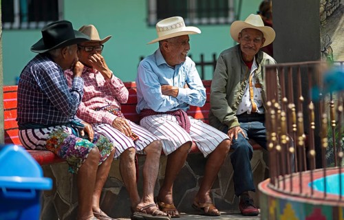Guatemalan men wearing Coxboy hats sitting laughing on a bench in Santiago de Atitlán, Sololá
