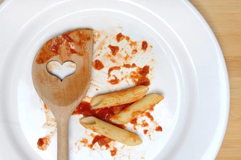 Plate with cooking spoon and leftovers from pasta, food waste