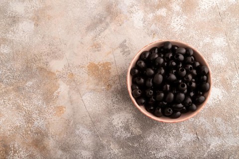 Fresh black olives in ceramic bowl on brown concrete background. Top view, flat lay, copy space