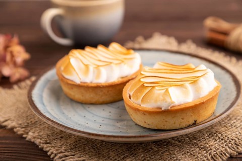 French lemon tart with meringue on brown wooden background, cup of coffee, linen textile, side