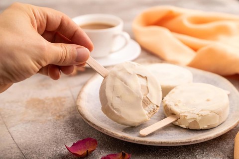 ?hocolate Ice cream in white glaze, cup of coffee, with hand on brown concrete background and