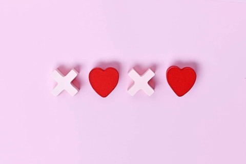 Valentine flat lay with wooden light pink and red hearts forming XOXO letters arranged on a pink