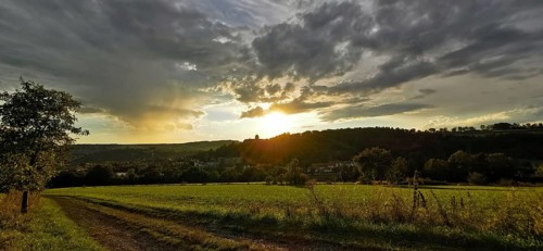 A rural scene with meadows and dirt roads at sunset, dramatic cloud formations, Franconian Forest