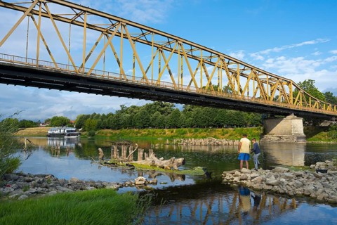 Yellow metal bridge across river with two anglers on the shore and blue sky, bridge over Morava