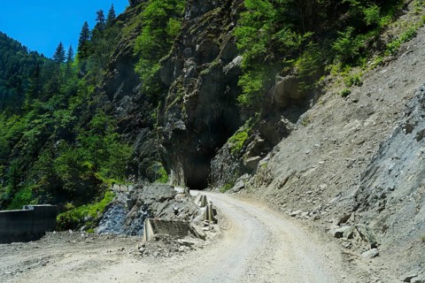 Gravel road winds around rocky mountain walls near a tunnel, road 7 partly slipped down, west of
