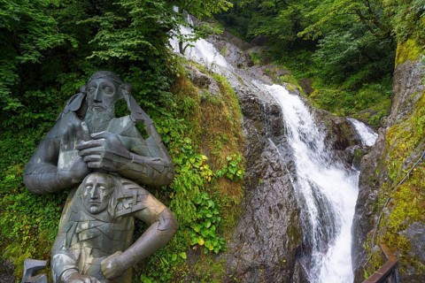 Sculpture in the forest next to a rushing waterfall, statue of Saint Andrew and waterfall of Saint