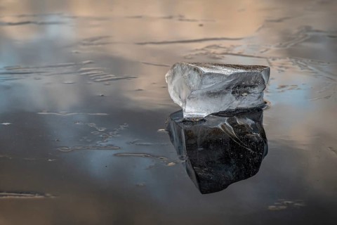 A piece of ice lies on the frozen surface of a lake in which clouds are reflected, Finland