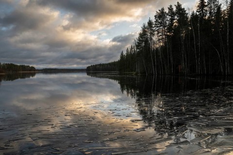 Pieces of ice and clouds reflecting on the water surface, lake in a forest, winter, Finland