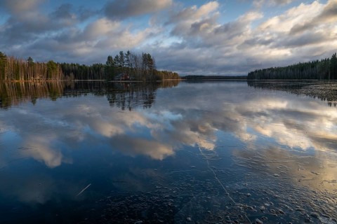 Ice and clouds reflecting on the water surface, lake in a forest, Finland