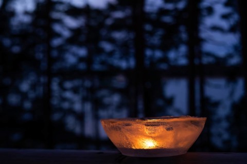 Ice bowl illuminated by burning tea light stands on balcony balustrade, forest at the onset of