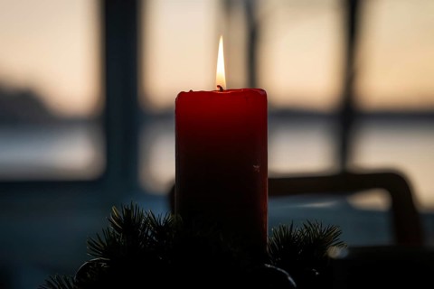 A single red candle in an advent wreath burns in front of a window at dusk and creates a cozy